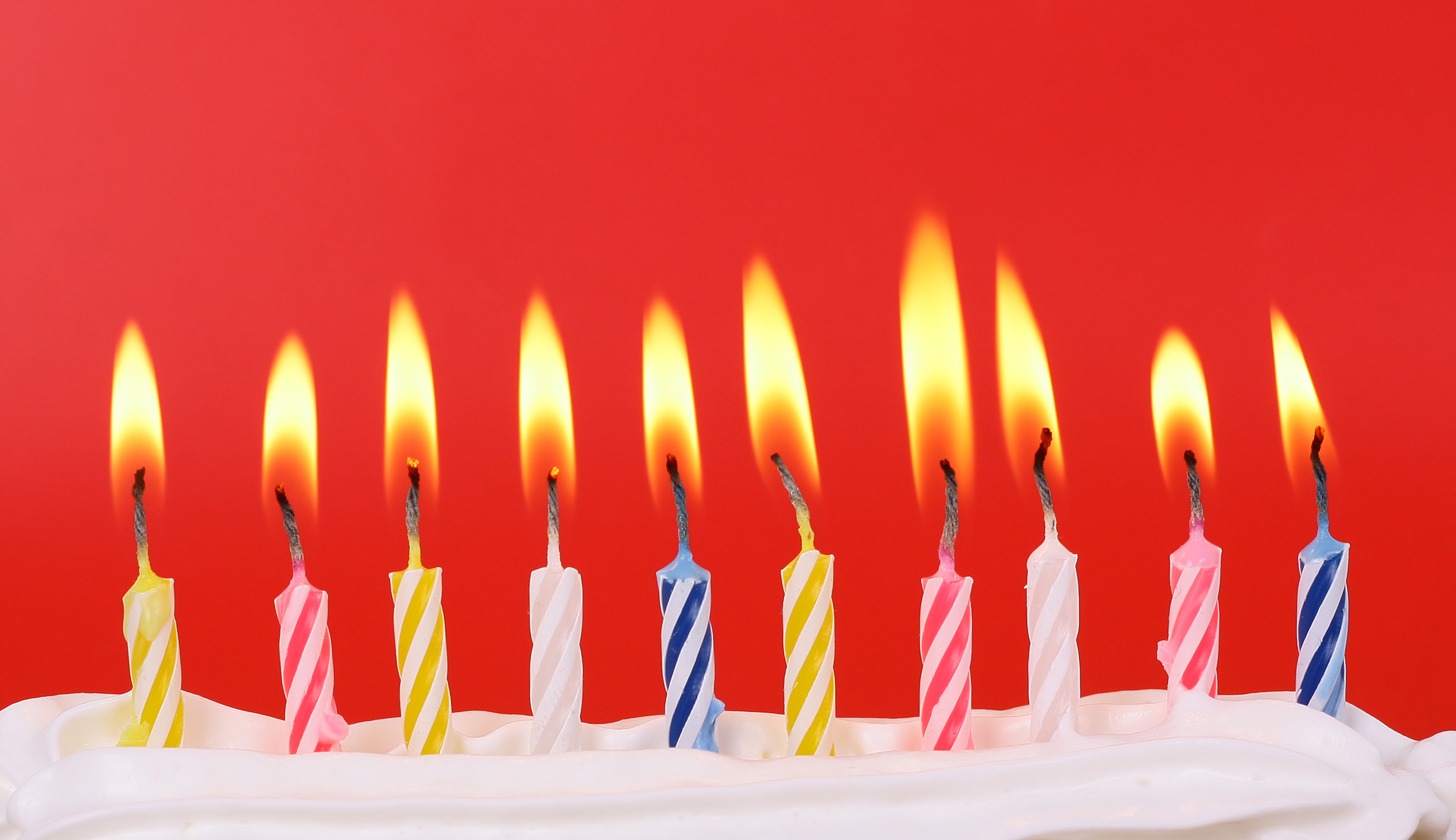 Row of ten colorful birthday candles lit on a red background